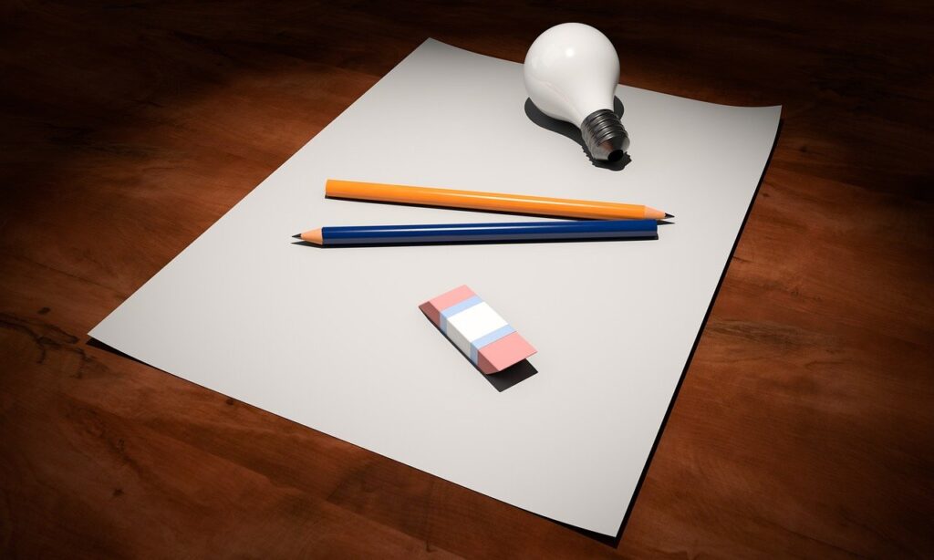 On top of a white piece of paper, there is a lightbulb, an orange colored pencil, a blue colored pencil, and an eraser. 